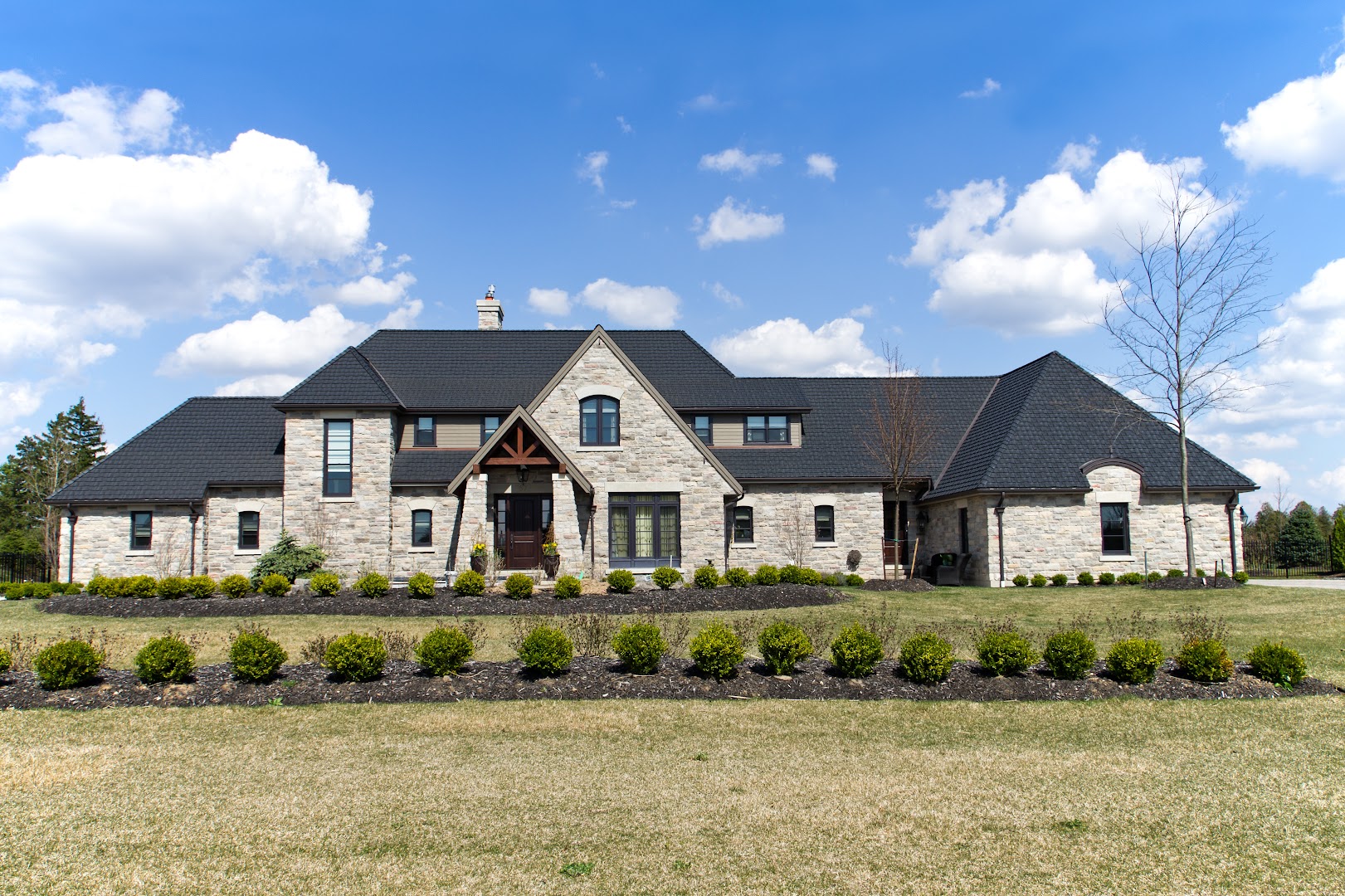 Large stone estate home with dark shingle roof